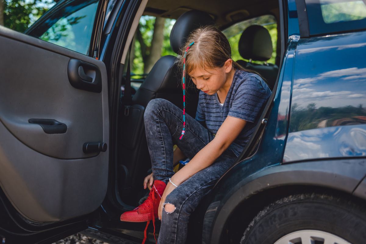Young girl sitting in the backseat of a car putting on red sneakers